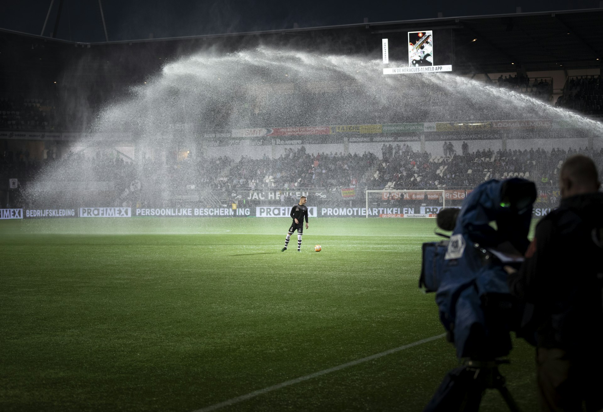 Stadium sprinklers watering a floodlit pitch